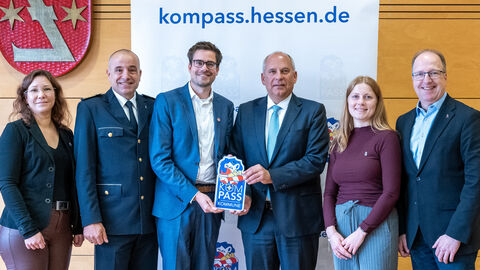 Innenminister Roman Poseck u.a. mit Polizeipräsident Björn Gutzeit, Bürgermeister Carsten Sinß und Landtagsabgeordneter Ingo Schon  Sechs Personen stehen nebeneinander - zwei halten ein kleines Schild mit der Aufschrift "Kompass" in den Händen.